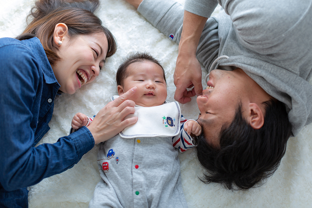 横になって赤ちゃんを見ている家族の写真