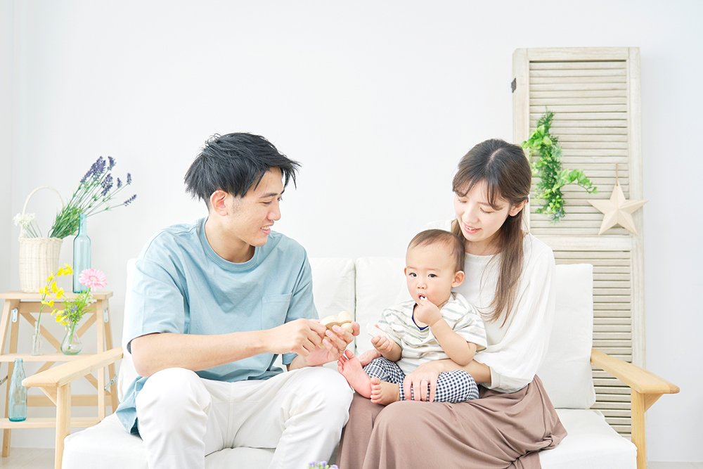 赤ちゃんを抱いた若い夫婦が、ソファに座っている写真