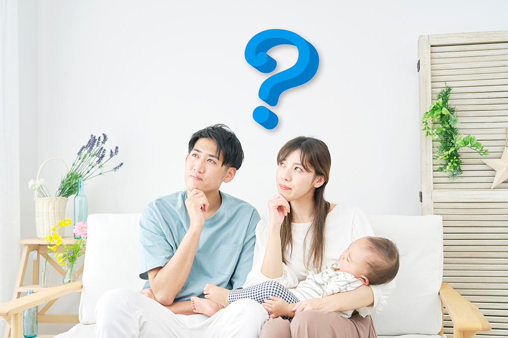 赤ちゃんを抱いた若い夫婦が、ソファに座って悩んでいる写真